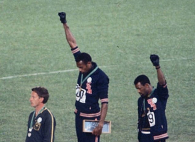 Gold medalist Tommie Smith (center) and bronze medalist John Carlos (right) showing the raised fist on the podium after the 200 m race at the 1968 Summer Olympics; both wear Olympic Project for Human Rights badges.